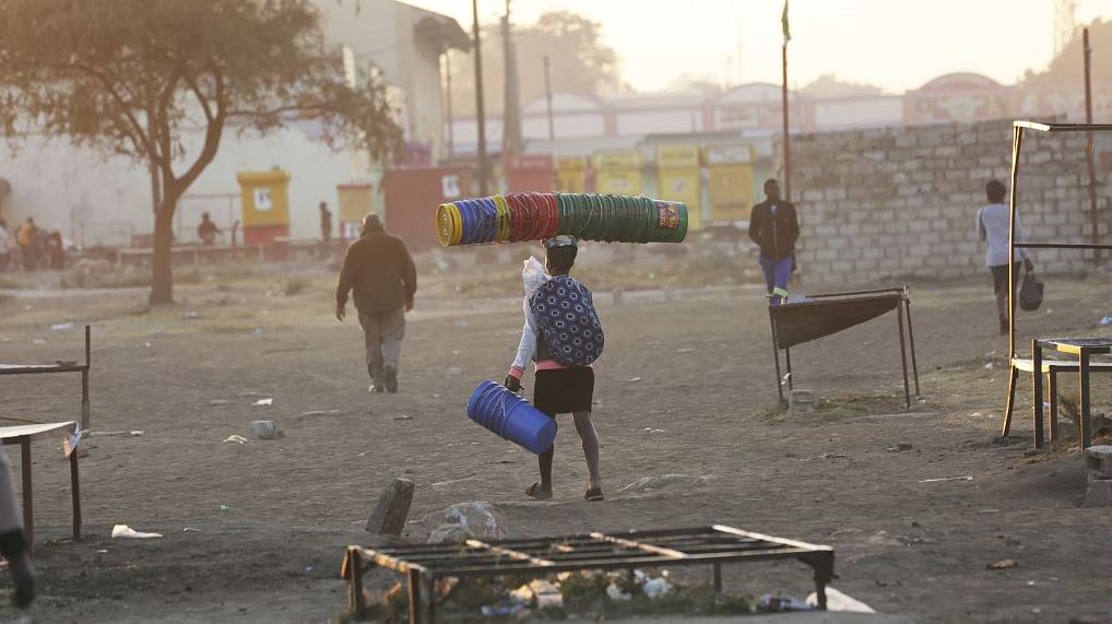 FILE: A woman carries empty buckets and a baby on her back in the early morning on the dusty streets of Lusaka, Zambia, Monday, July, 5, 2021. /CFP