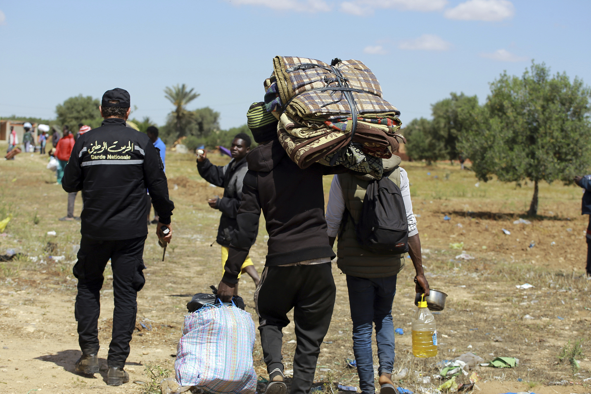 Sub-Saharan migrants carry their belongings after the makeshift camp where they were staying was dismantled by authorities, at al-Amra, on the outskirts of the Tunisian port city of Sfax, Thursday, April 24, 2025. /CFP