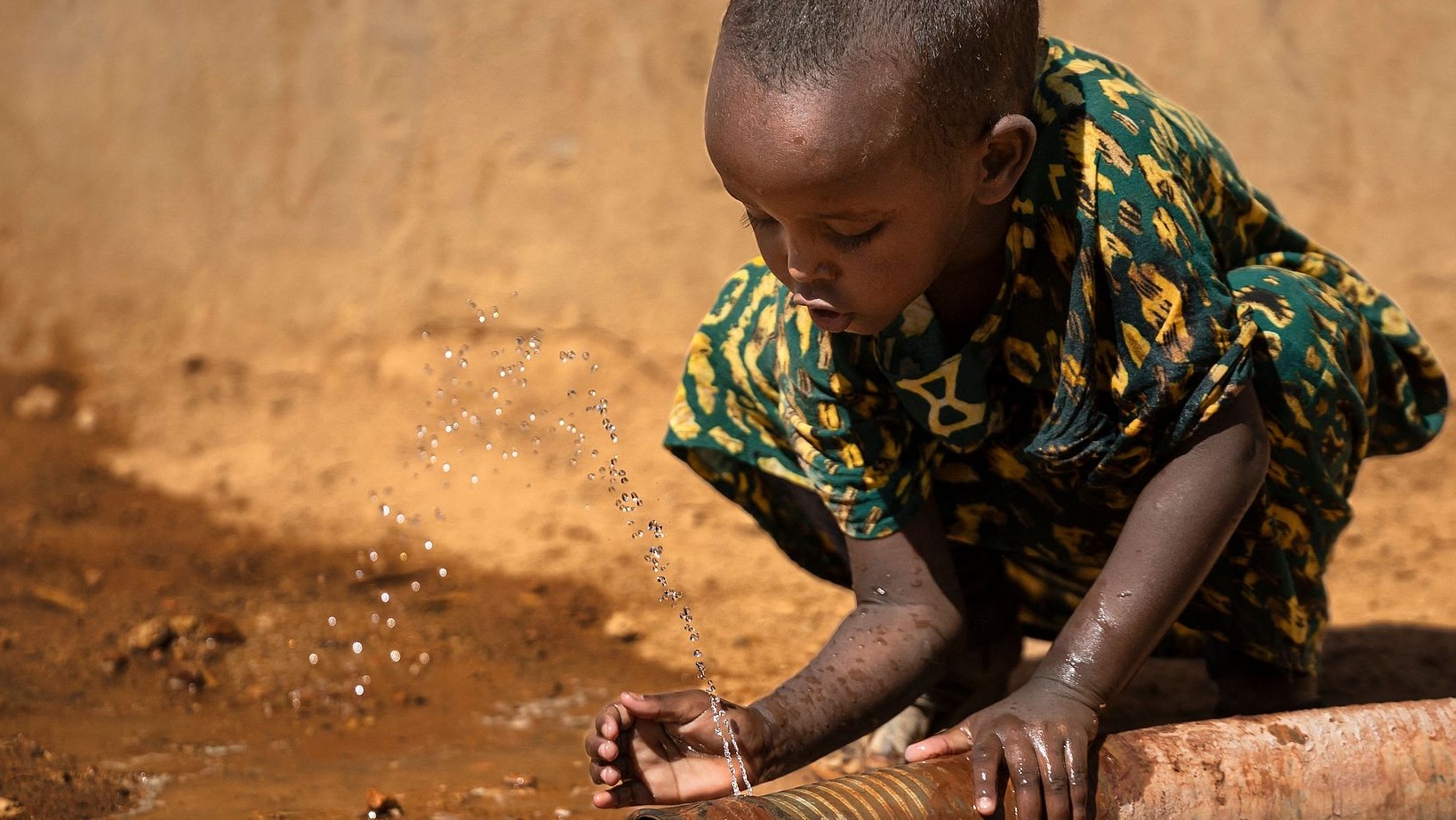 A little girl drinks water from a leaking water pipe in a waterwheel in Hawala village near Lamu, Kenya, January 21, 2026. /CFP