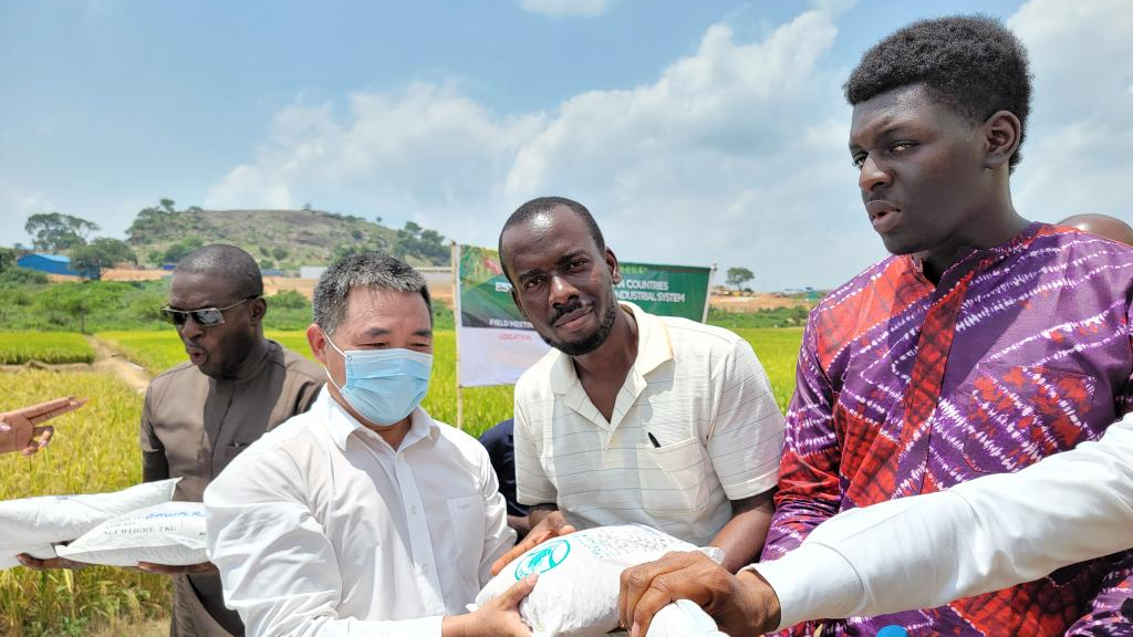 Chinese agriculture expert Wang Xuemin (2nd L) hands over rice seeds to local people at a demonstration farm operated by a Chinese firm in Abuja, Nigeria, June 2, 2022. /Xinhua