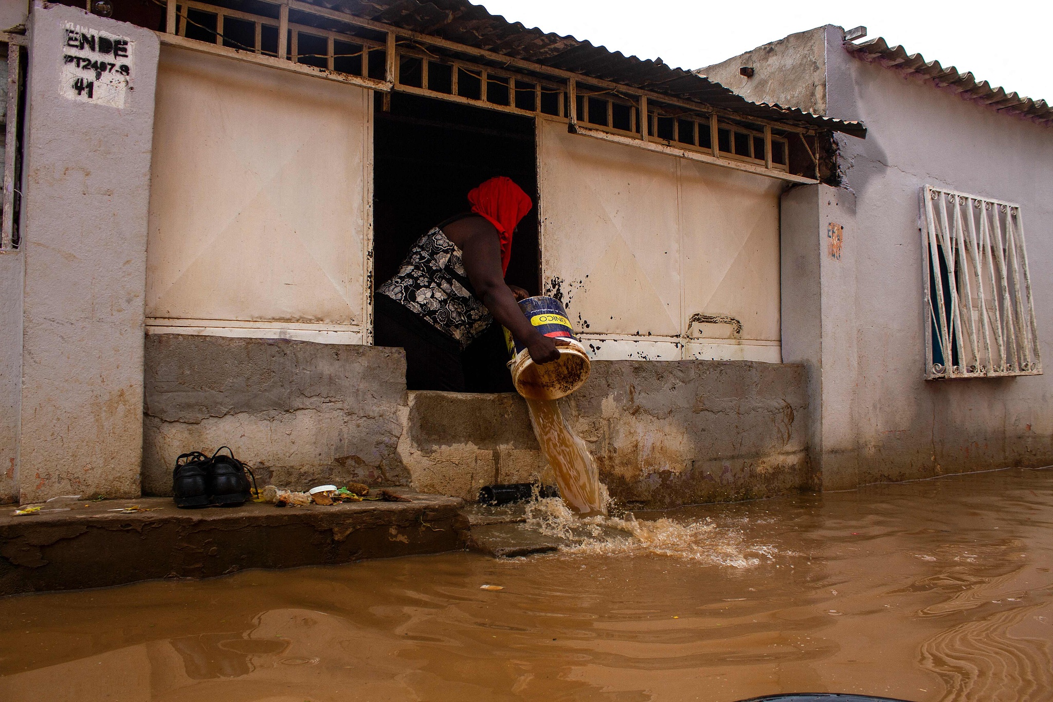 FILE: A resident, throws out floodwater from her house, in the Futungo District of Luanda, Angola, on April 19, 2021. /CFP