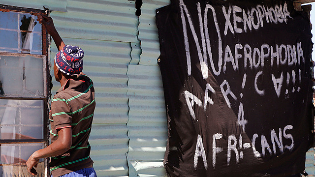 A man replaces a broken window in Philippi township, Cape Town, South Africa, April 20, 2015, next to a banner that reads: 