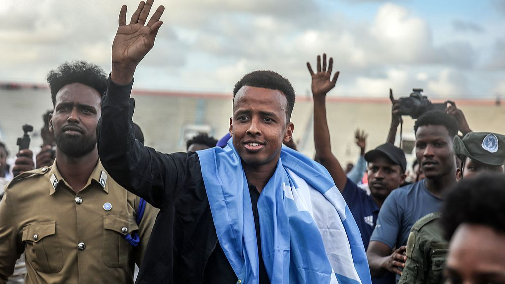 Somali international referee Omar Abdulkadir Artan waves to supporters while draped in the Somali flag as he is welcomed in Mogadishu ahead of a solidarity football match on June 10, 2026, after returning to Somalia. /CFP
