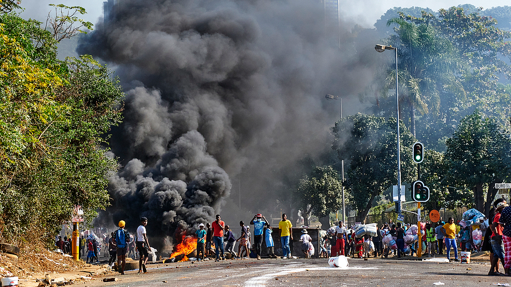 Looters outside a shopping center alongside a burning barricade in Durban, South Africa, July 12, 2021. /CFP