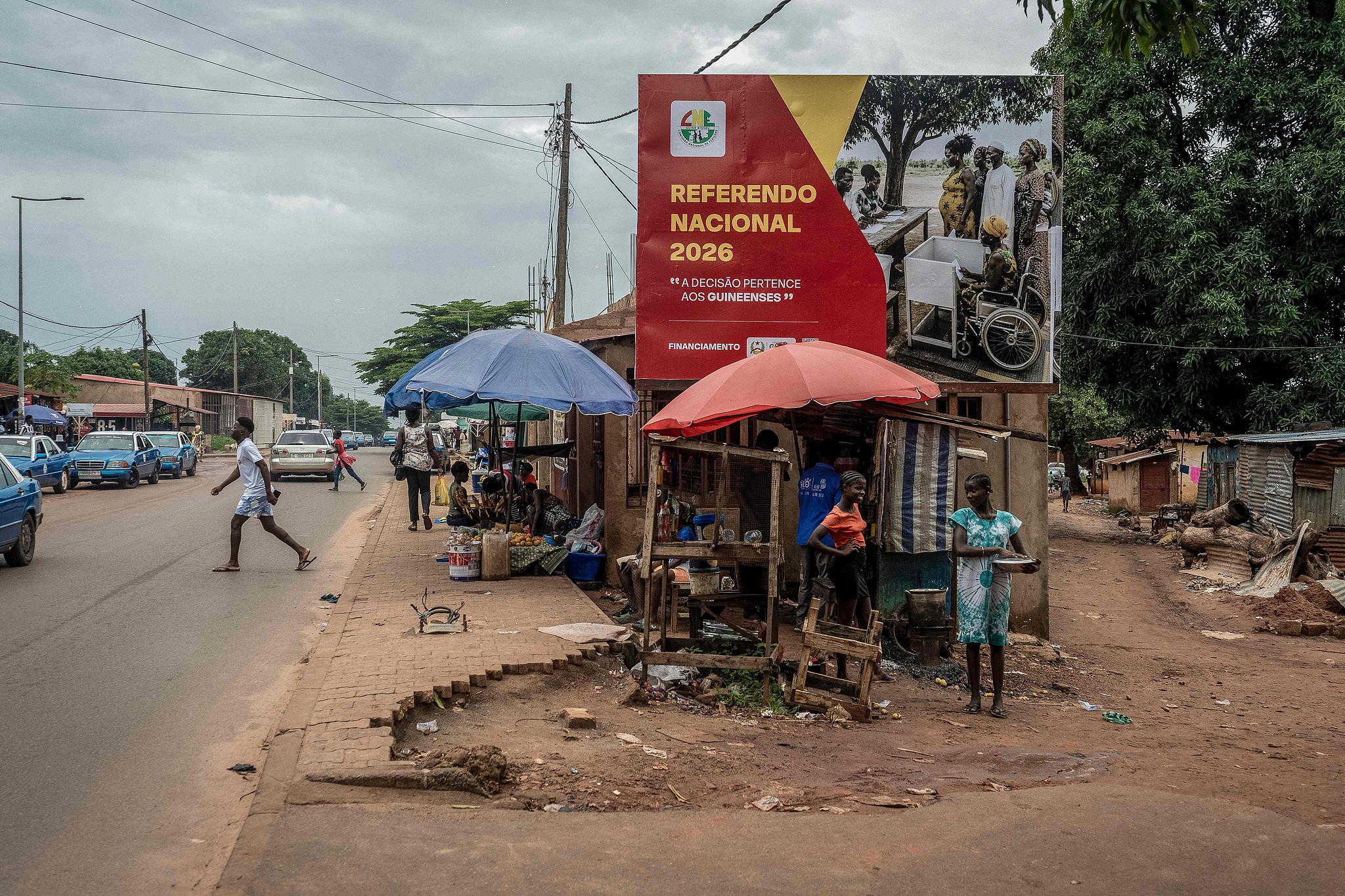 People stand near a campaign billboard calling to vote in a referendum in Antula, near Bissau, on August 20, 2026. /CFP