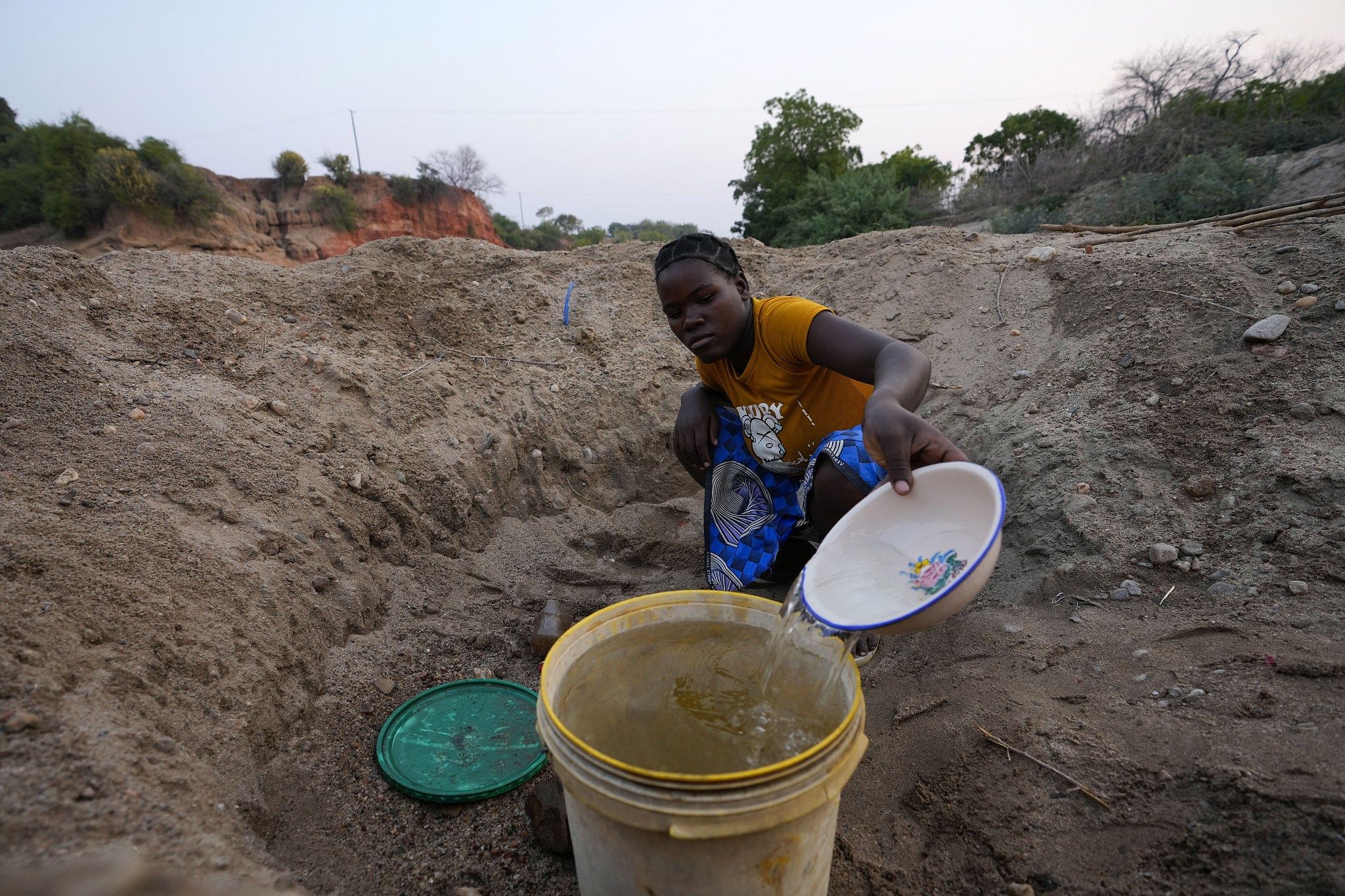 A woman scoops water from a hole she has dug in a dried up riverbed in Lusitu, Zambia, Wednesday, September 18, 2024. /CFP